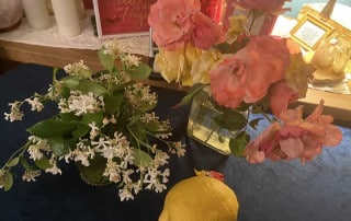 flowersndlemon | Ann Albers Visions of Heaven Colorful arrangement of pink and yellow roses in a glass vase with white blossoms nearby, and a lemon on a dark table in the foreground.