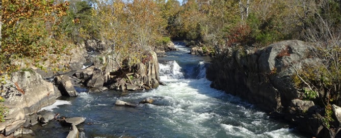 Autumnal river winds through a rocky gorge with small waterfalls and colorful trees along the banks.